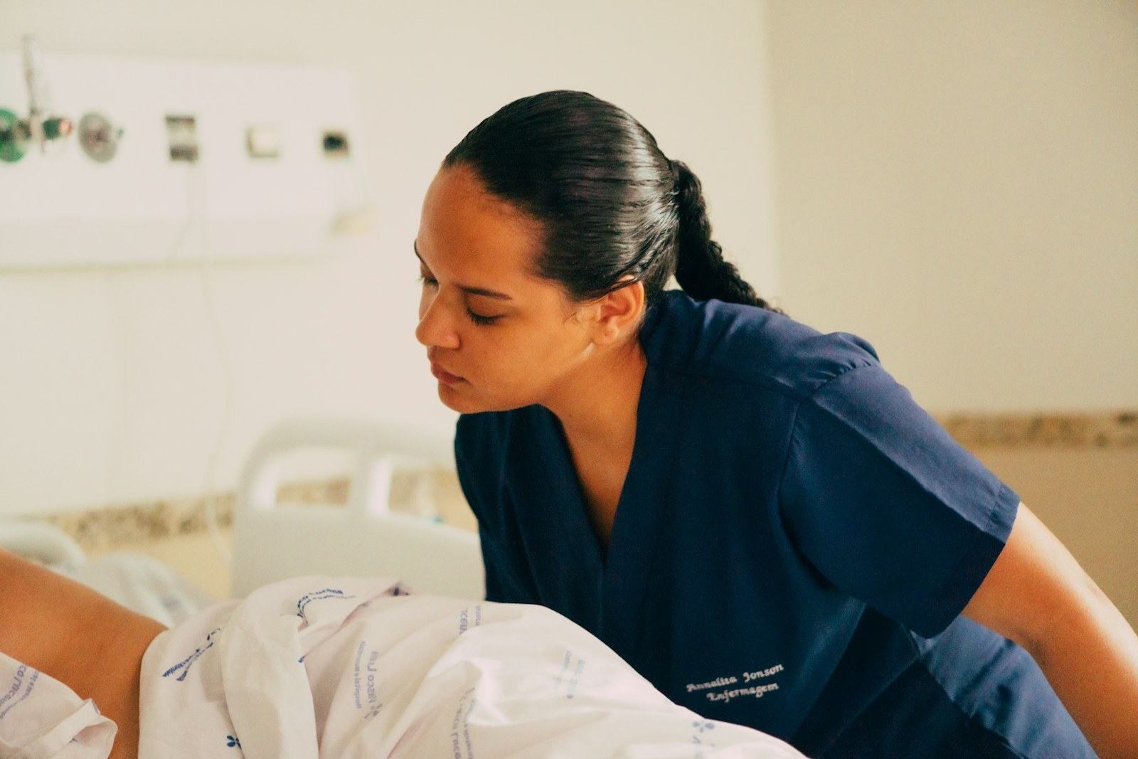 A carer in navy scrubs leaning in to check on someone resting in bed