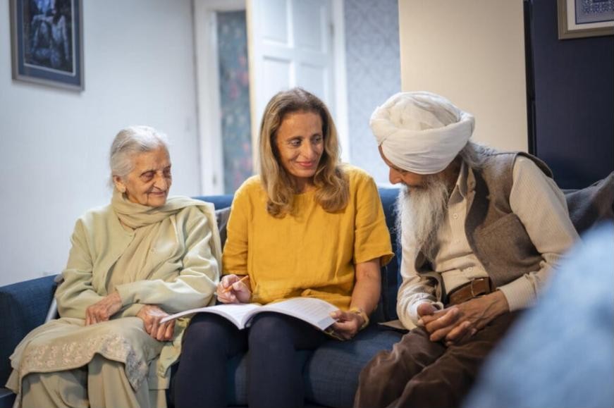 An older Sikh couple at home on the sofa, going through some paperwork with a care worker