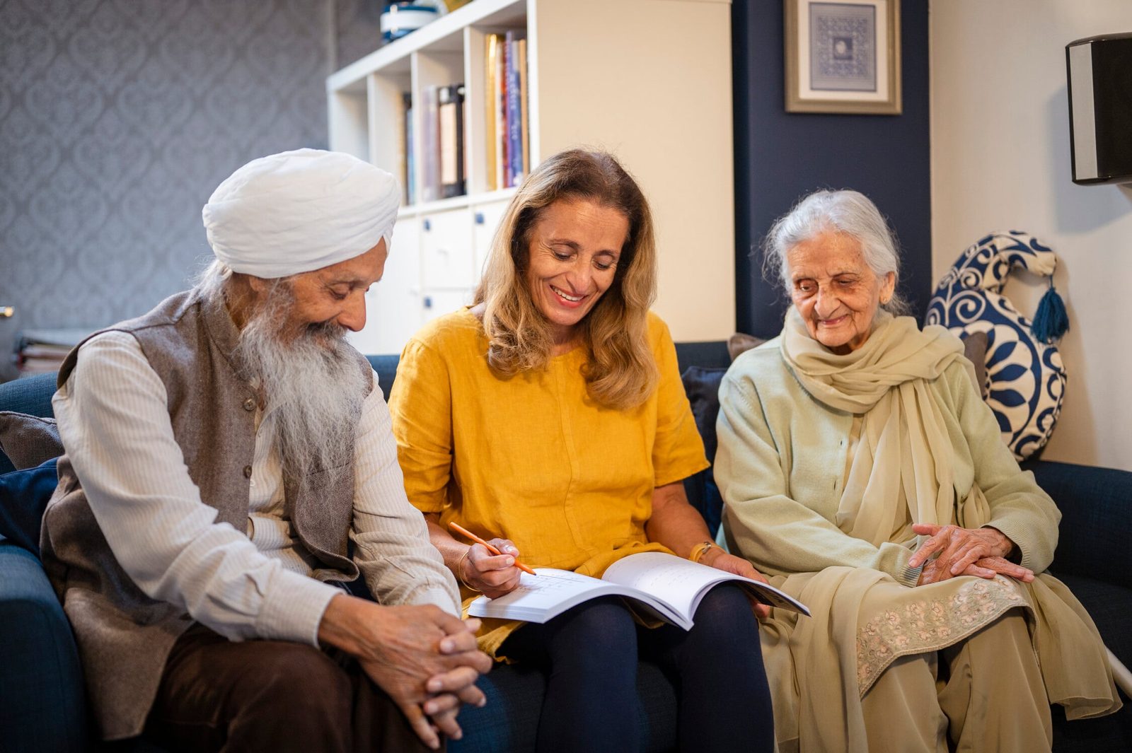 A visitor sitting on the sofa with an older couple, helping them with some paperwork at home